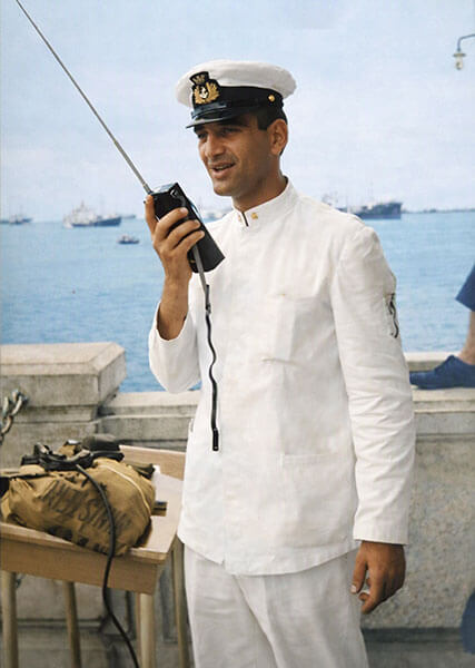 Vittorio Russo in uniforme navale bianca mentre utilizza una radio portatile (ricetrasmettitore) d'epoca sul molo del porto di Singapore - Novembre 1964